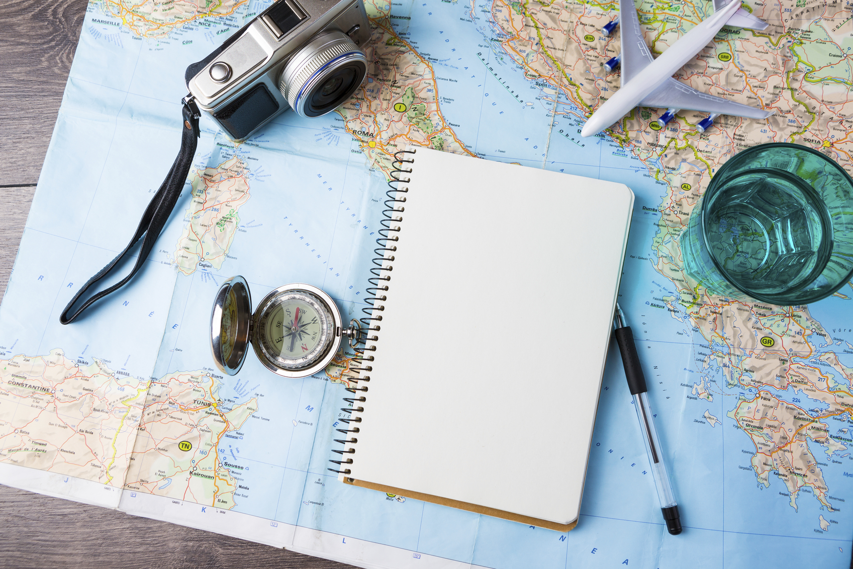 travel tourism agency table mockup tools compass, glass of water note pad, pen and toy airplane and touristic map on wooden table. Empty space you can place your text or information.